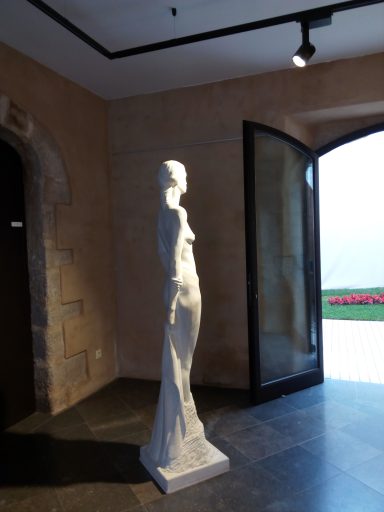 Escultura blanca de pie en un interior, con una puerta abierta al fondo.
